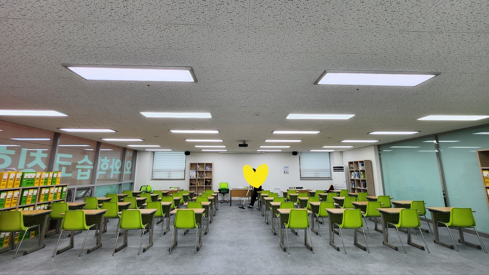 옥정점 넓은 학습실 전경 — 연두색 의자와 책상이 여러 줄로 가지런히 놓여 있고 천장에는 긴 조명이 이어져 있다. 왼쪽 벽면에는 파일박스가 꽂힌 수납장과 분홍색 브랜드 월이, 안쪽에는 책이 꽂힌 책장 두 개가 보인다