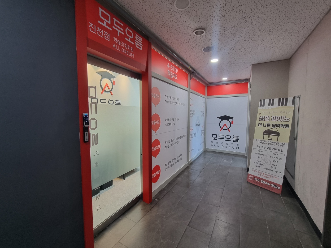 진천점 입구 복도 — 붉은색 출입문 옆으로 맞춤진단·맞춤지도·맞춤코칭·맞춤처방 4-STEP 학습지도 안내판이 벽에 붙어 있는 모습