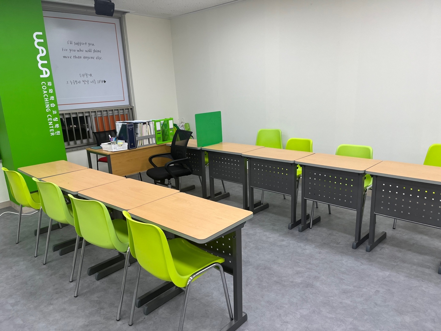 광주 광산구 월계동 와와학습코칭 첨단점 교실 — 초록 기둥의 WAWA 와와학습코칭학원 로고, 벽을 따라 한 줄로 놓인 책상과 연두색 의자, 창가의 코치 책상과 교재 파일꽂이
