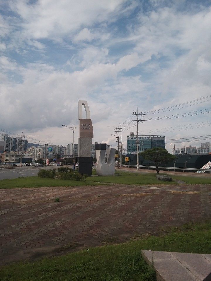 대구대학교 경산캠퍼스 입구 — 길가 잔디밭에 세워진 석조 조형물과 그 뒤로 보이는 시가지