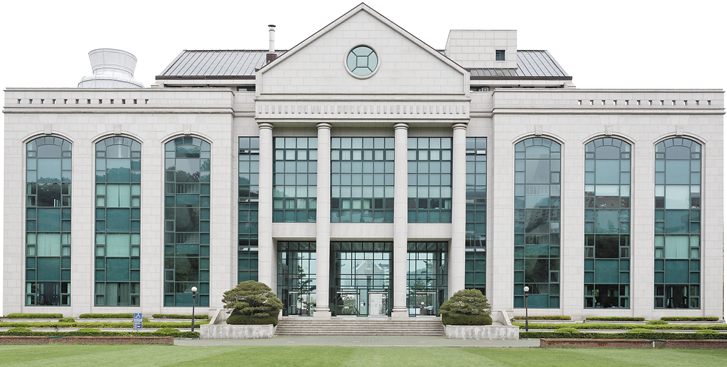 울산대학교 본관 — 가운데 삼각 박공과 원형 창, 흰 기둥이 늘어선 현관, 좌우로 아치형 유리창이 이어진 석조 건물과 앞쪽 잔디밭